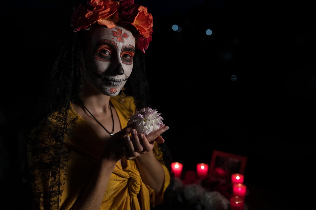 Woman with Catrina sugar-skull makeup celebrating Day of the Dead holding a white flower