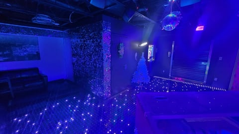 Futuristic nightclub interior with glowing blue LED floor, illuminated walls, and dark purple ambient lighting