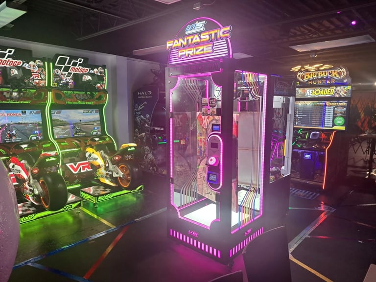 Neon-lit arcade game floor with glowing pink and green machines, including racing games and a central prize redemption booth