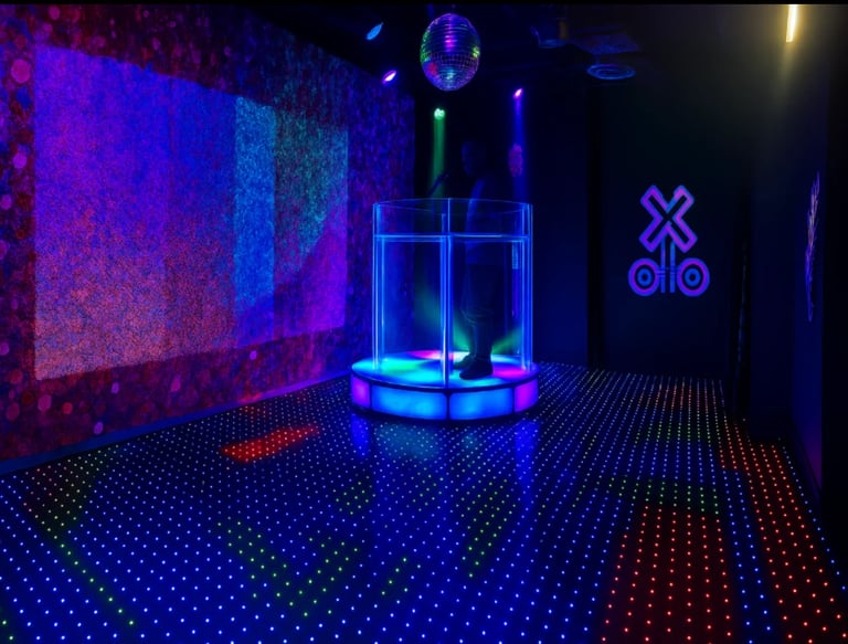 Futuristic neon-lit nightclub interior with LED dance floor, glowing blue cylindrical stage platform, purple wall panels, and neon logo signs