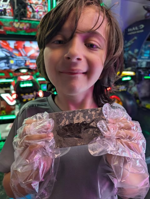 Child smiling at arcade holding a video game controller with pink decorative sleeves