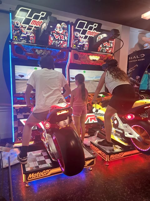 Children playing MotoGP arcade motorcycle racing games in an arcade room with neon lighting