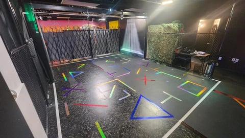 Modern indoor gym with colorful geometric floor markings, gym equipment on walls, and neon lighting for fitness training