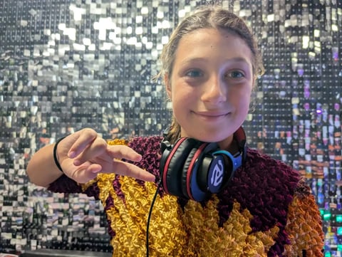 Young girl holding black and blue headphones around her neck in front of a sparkly sequin backdrop