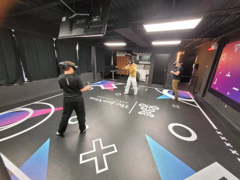 Interactive gaming experience with people standing on illuminated floor panel displaying symbols and colorful graphics in a dark room