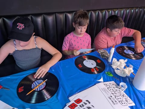 Three people seated at a blue table examining vinyl records and music memorabilia