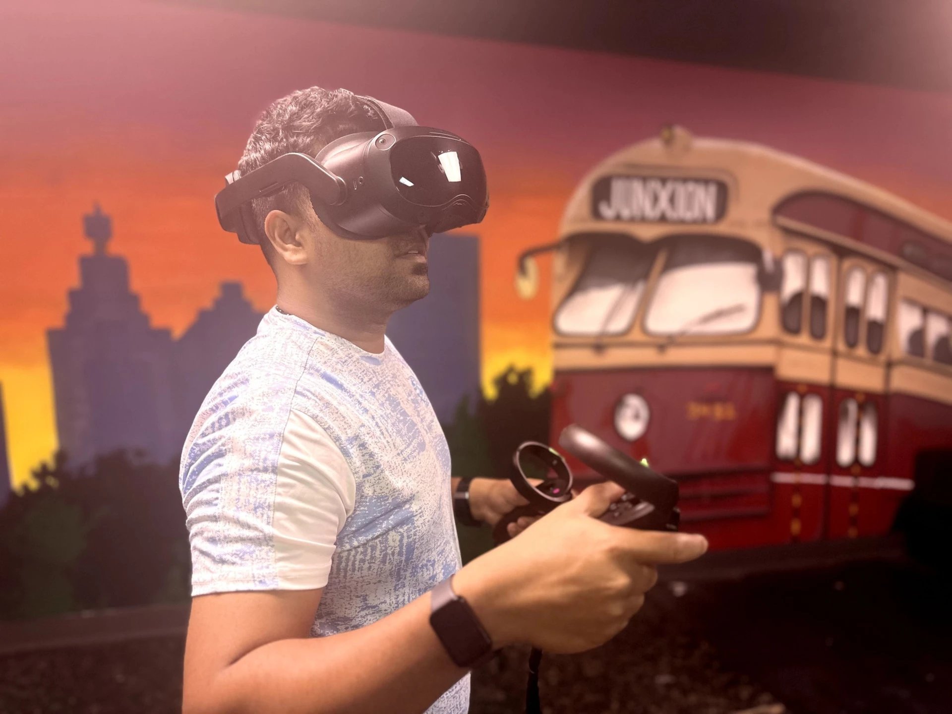 Person wearing VR headset holding controller with virtual train and sunset cityscape in background